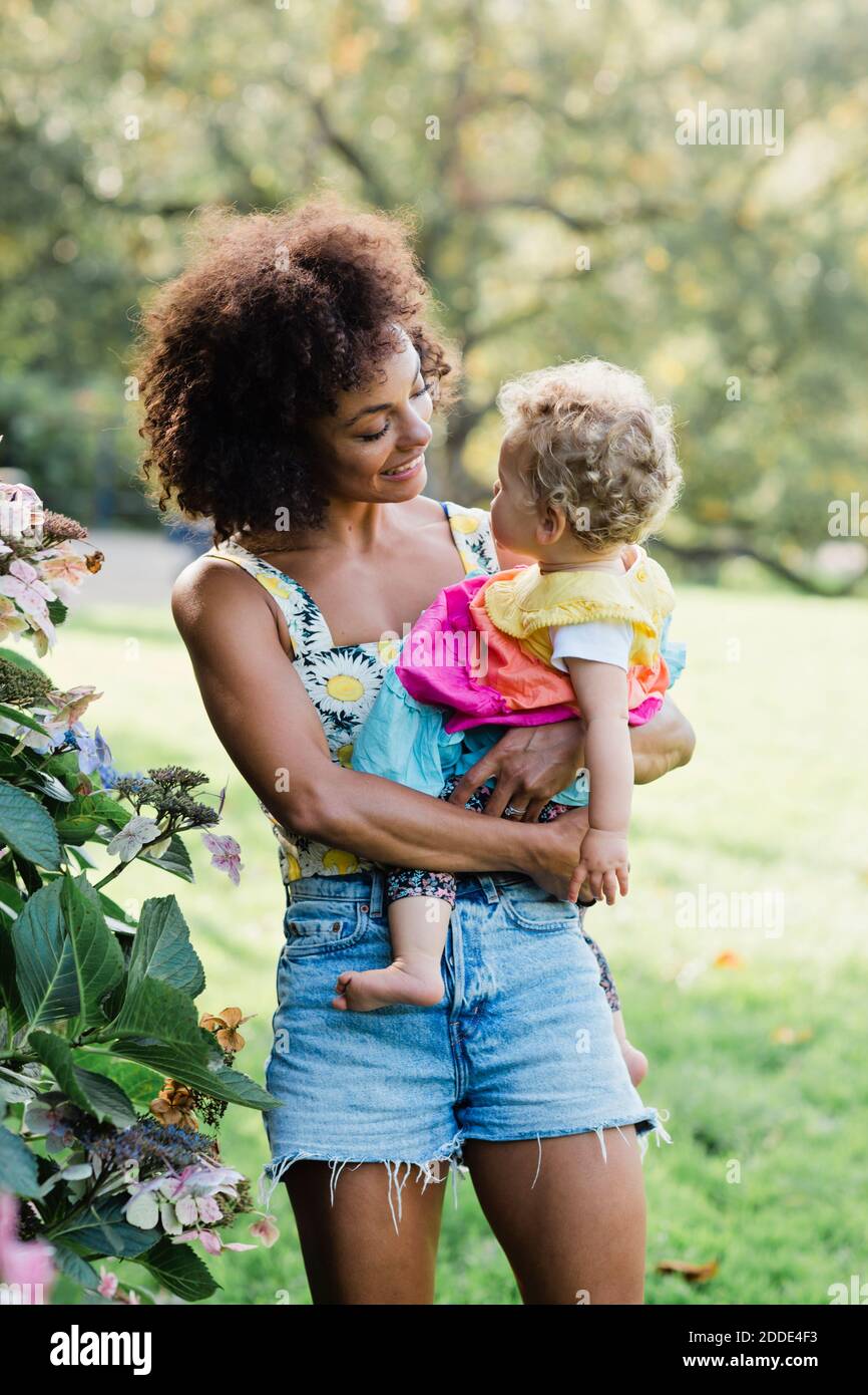 Lächelnde Mutter, die das Baby anschaut, während sie im Park steht Stockfoto