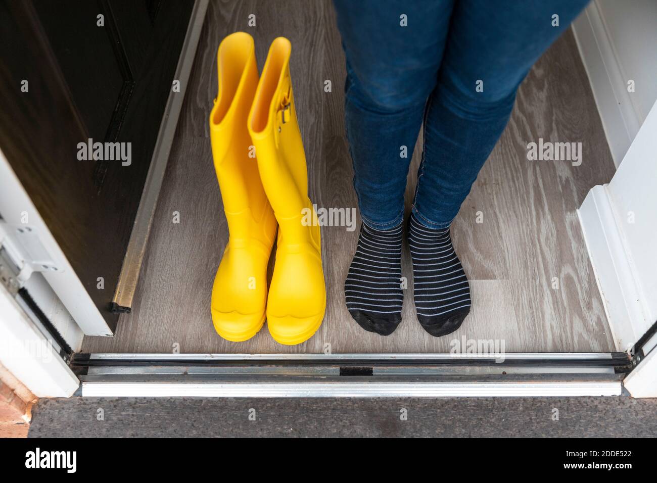 Beine der Frau stehen mit Gummistiefel an Tür Zu Hause Stockfoto