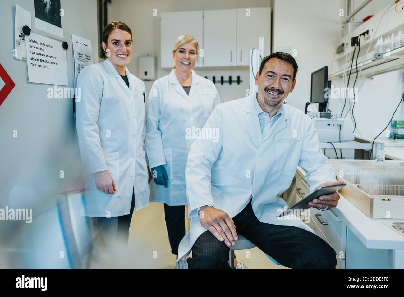 Wissenschaftler mit digitalem Tablet und Kollegen, die im Labor hinter sich stehen Stockfoto