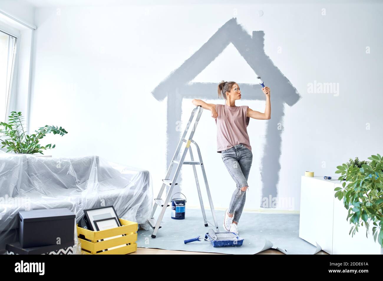 Junge Frau mit Farbe Roller tun Pout beim Anlehnen Leiter zu Hause Stockfoto