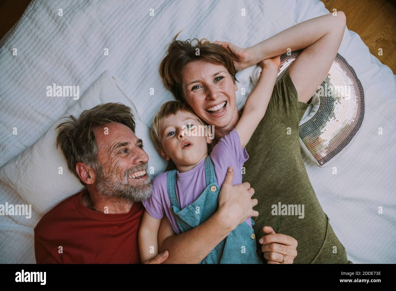 Lächelnde Mutter, Vater und Sohn liegen zu Hause auf dem Bett Stockfoto