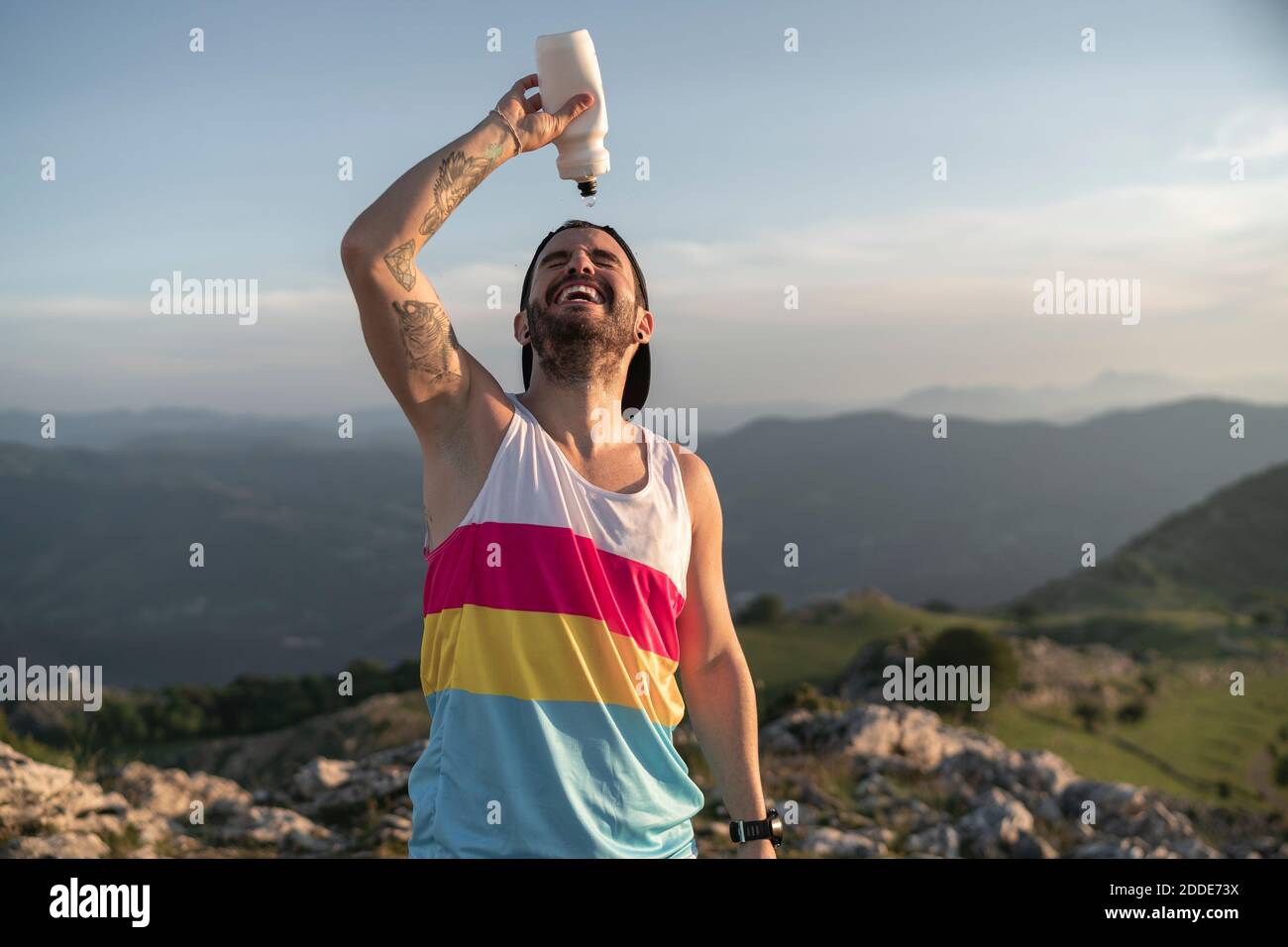 Athlet gießt Wasser auf das Gesicht, während auf dem Berg gegen stehen Der Himmel ist klar Stockfoto