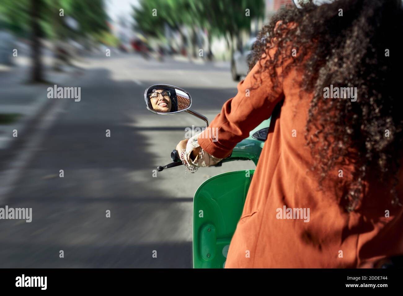 Lächelnde Frau Reflexion auf der Seite Blick Spiegel während der Fahrt Motor Roller in der Stadt Stockfoto