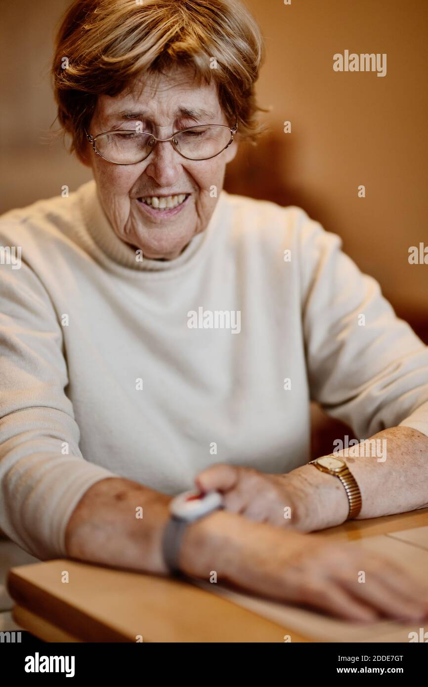 Faltige Frau, die den Notausschalter am Handgelenk über den Tisch drückt Zu Hause Stockfoto