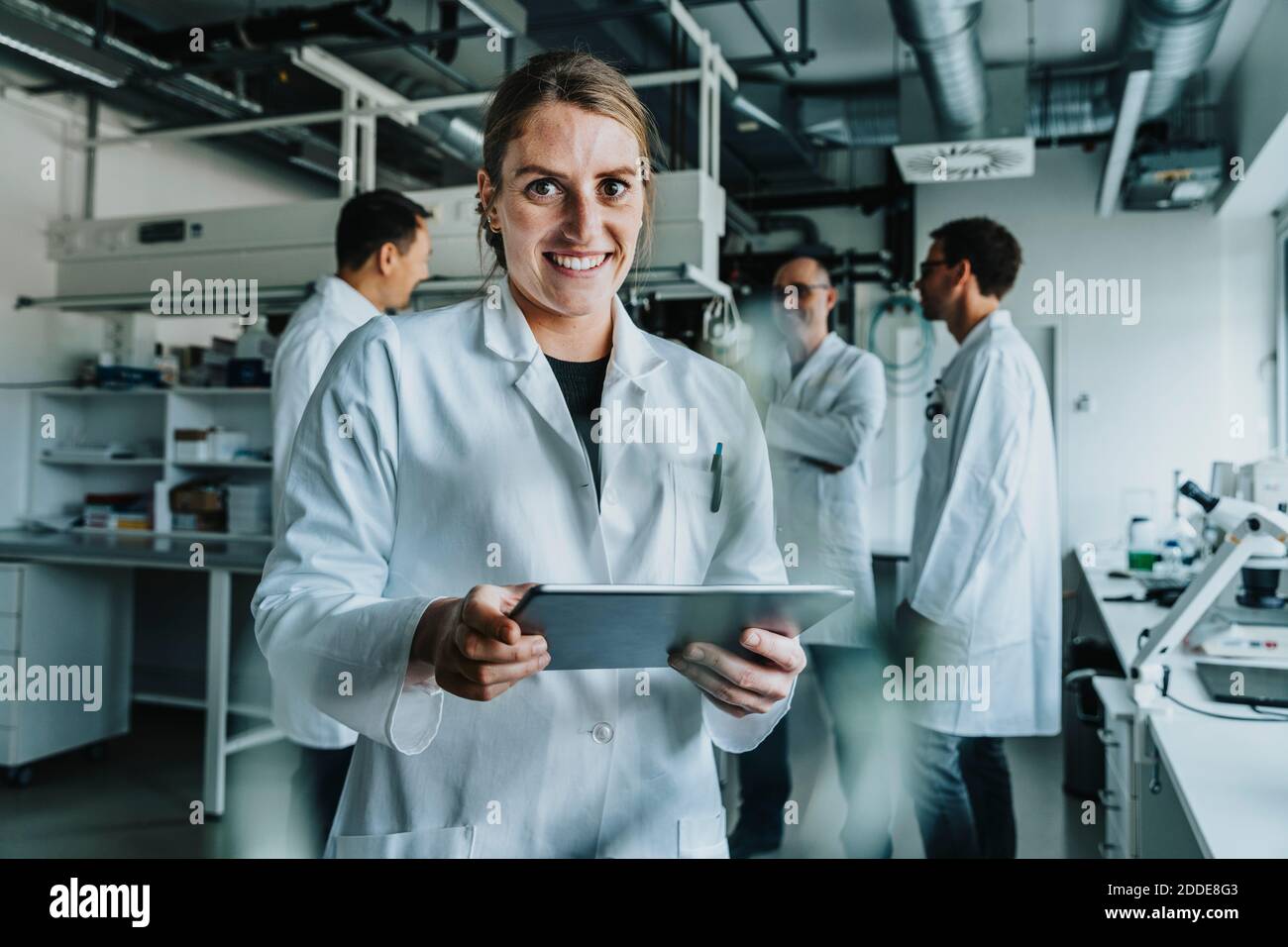 Lächelnde Frau mit digitalem Tablet, während sie mit einem Kollegen im Stehen steht Hintergrund im Labor Stockfoto