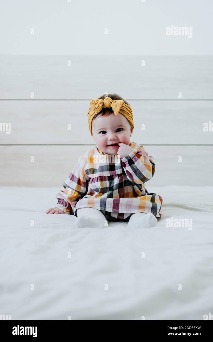 Nettes Baby Mädchen mit Finger im Mund auf dem Bett sitzen Zu Hause Stockfoto