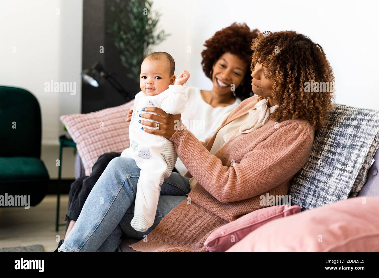 Lächelnde Familie sitzt mit Baby Mädchen auf dem Sofa zu Hause Stockfoto