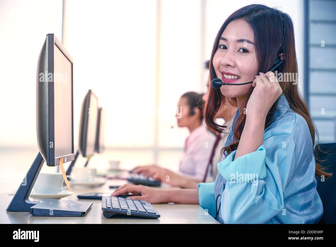 Junge Kundendienstmitarbeiterinnen mit Headsets und Computer arbeiten im Büro. Professionelles Bedienkonzept. Stockfoto