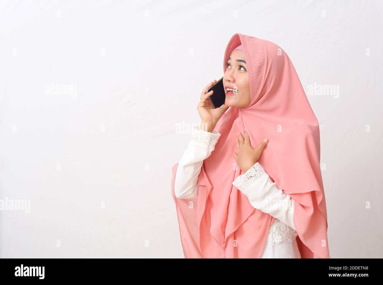 Ein Porträt einer glücklichen asiatischen muslimischen Frau, die einen Schleier oder Hijab trägt, während sie am Telefon spricht und ein nettes Gespräch mit jemandem hat. Isoliert auf Weiß Stockfoto