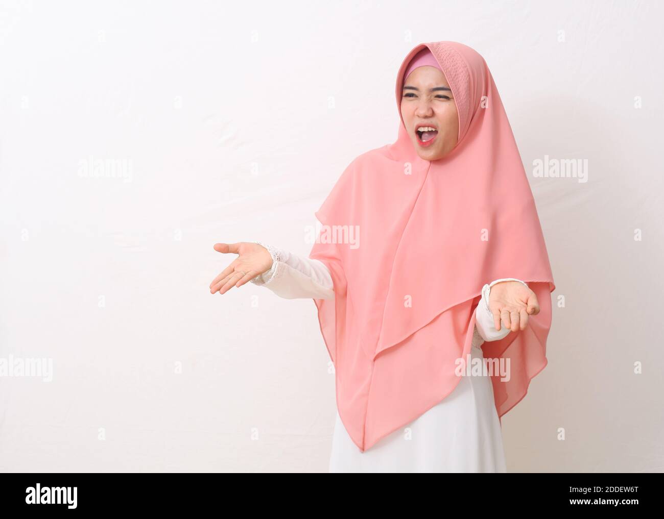 Asiatische muslimische Frau in einem rosa Schleier oder Hijab und weißen Kleid fühlt sich verrückt und verrückt schreien und mit aggressivem Ausdruck und Arme angehoben. Frustr Stockfoto
