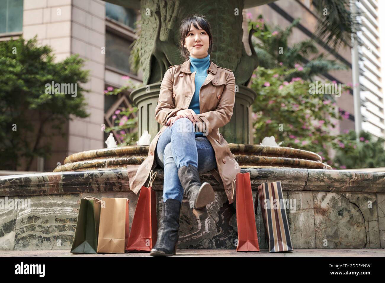 Junge asiatische Frau sitzt im Freien mit Einkaufstaschen an den Füßen Stockfoto