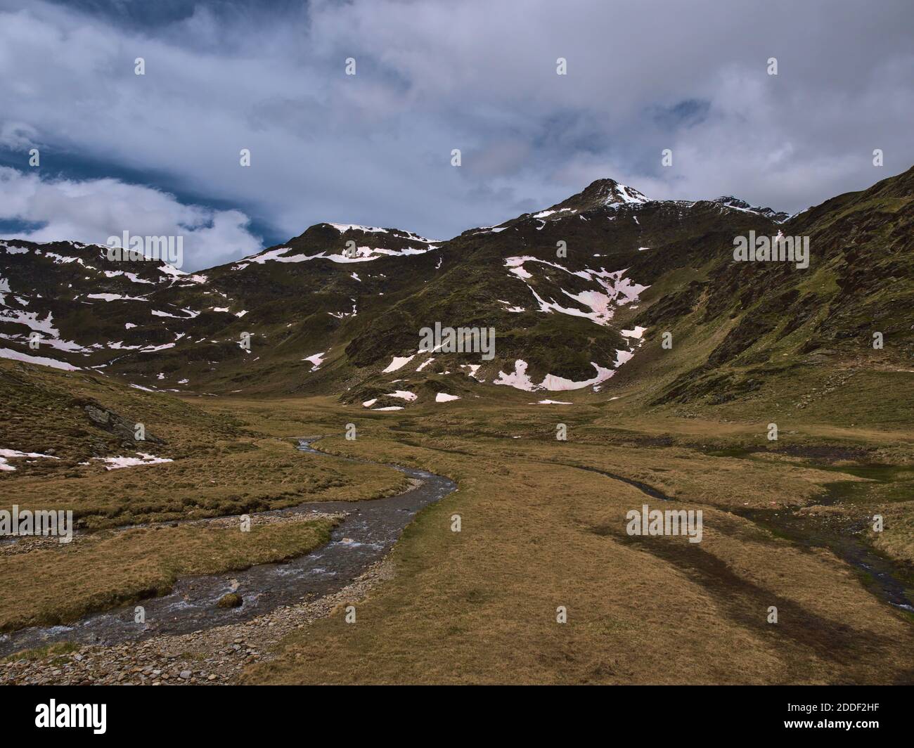 Karge Berglandschaft im Frühsommer mit Dampf aus Schmelzwasser, Wiesen und dem schneebedeckten Gipfel des Großen Degenhorns (2.946m) in den Alpen. Stockfoto