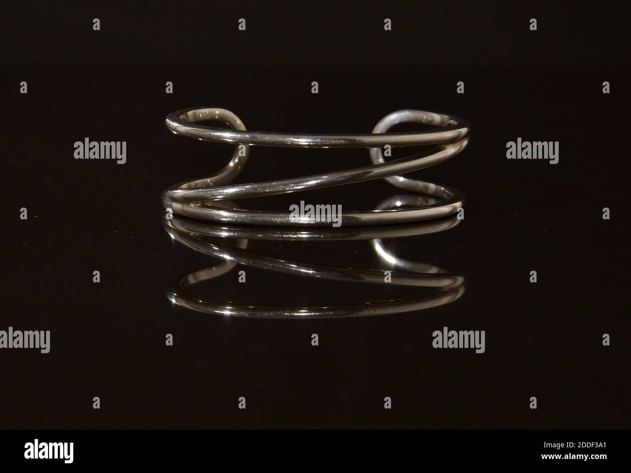 Moderner silberner Armreif auf einer glänzenden schwarzen reflektierenden Oberfläche. Stockfoto