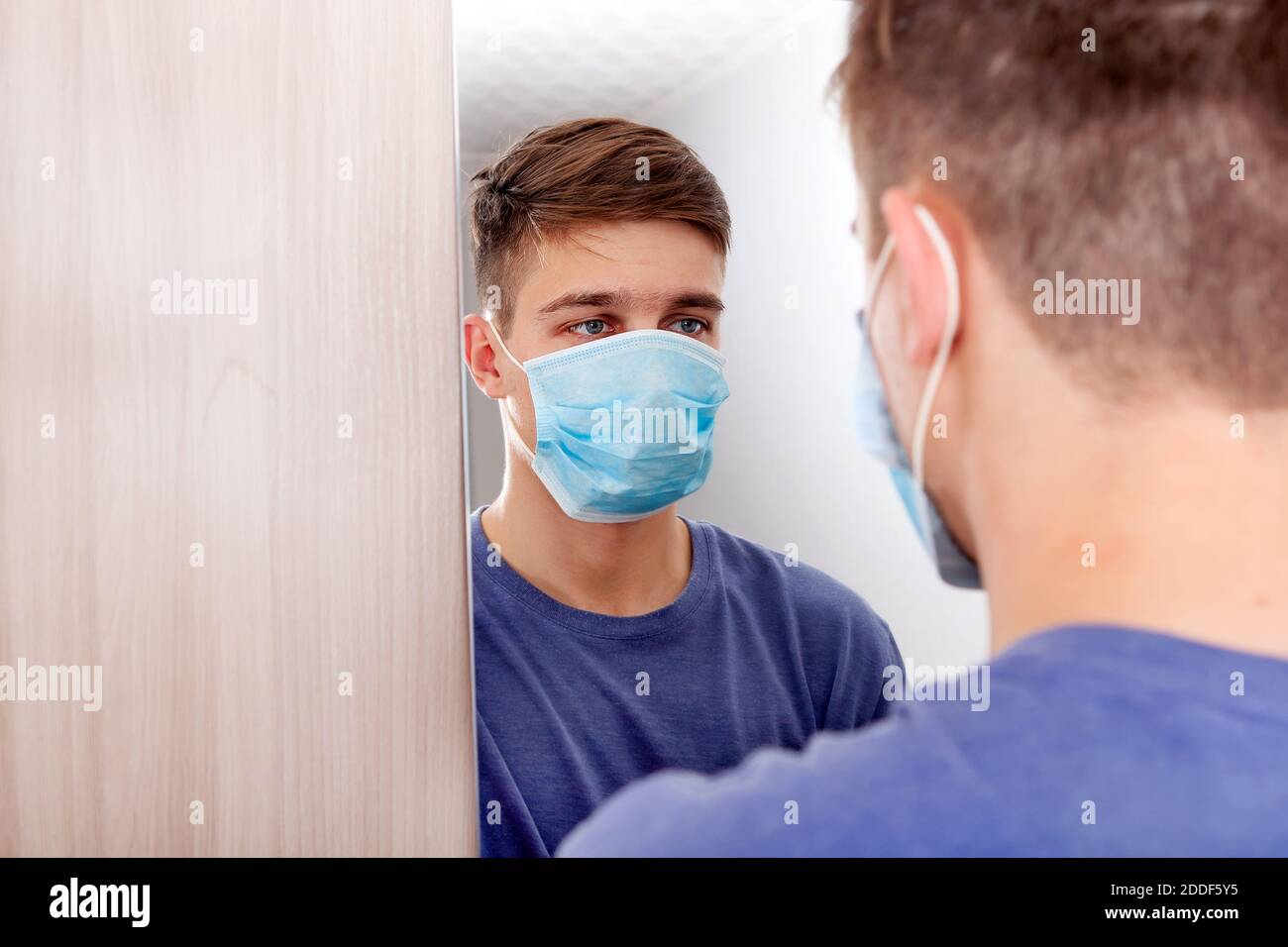 Junger Mann in Grippe-Maske Blick auf Reflexion in der Spiegel im Zimmer Stockfoto