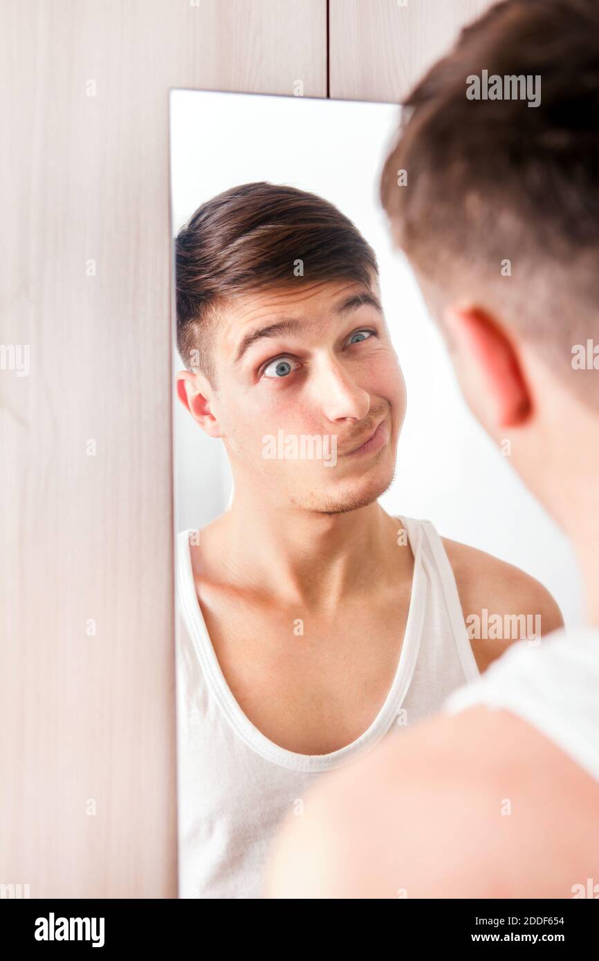 Junger Mann, der im Spiegel reflektiert und macht Ein lustiges Gesicht Stockfoto
