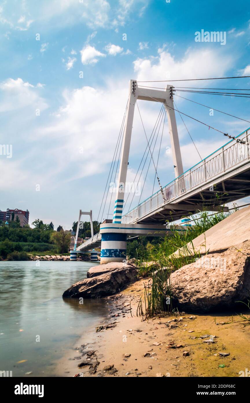 Die Fußgängerbrücke über den Fluss ist unter dem blauen Himmel mit einer Hängebrücke ausgestattet Himmel mit Wolken Stockfoto