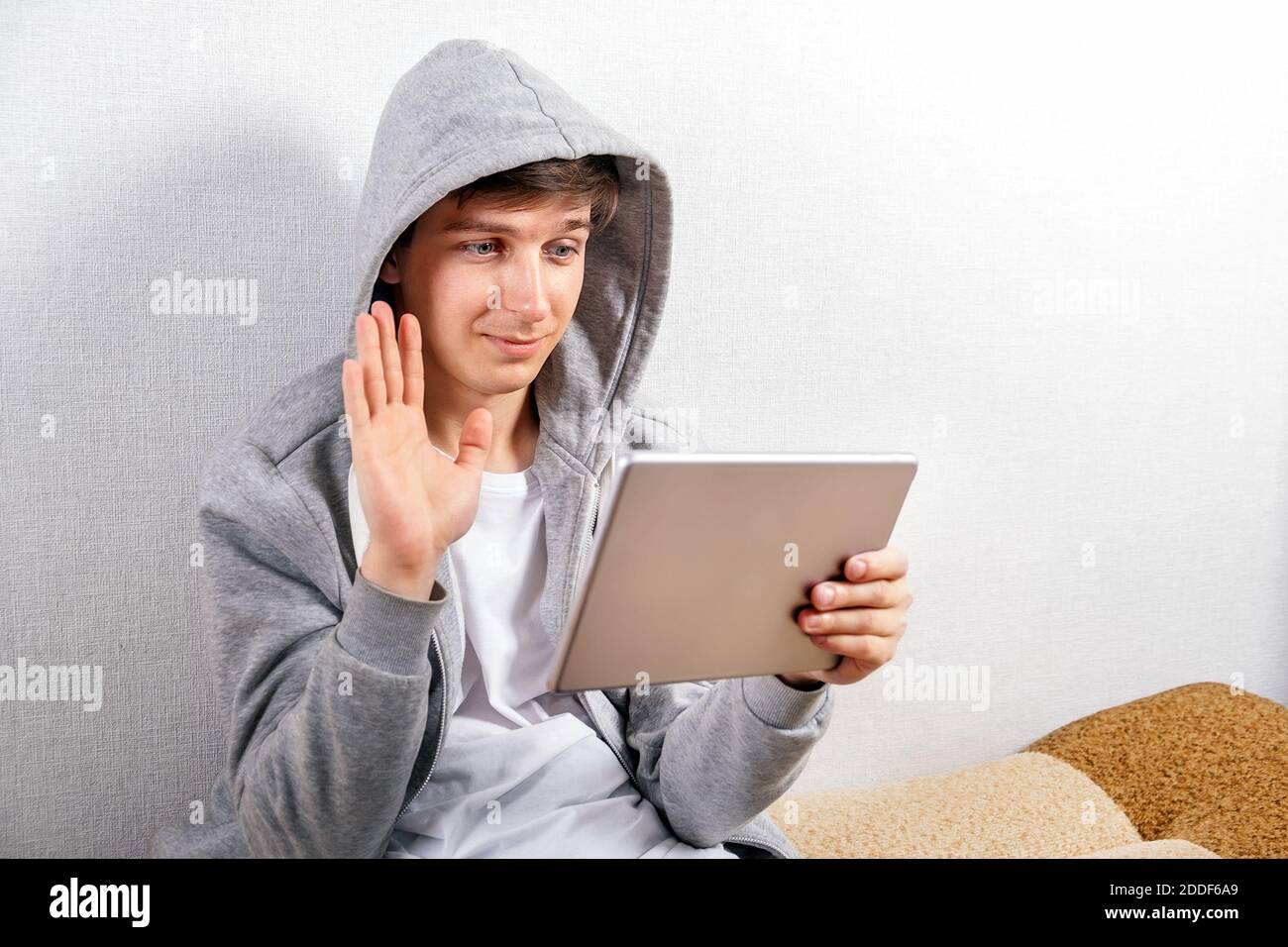 Junger Mann mit Tablet-Computer Welle mit einer Hand auf Das Sofa im Haus Stockfoto