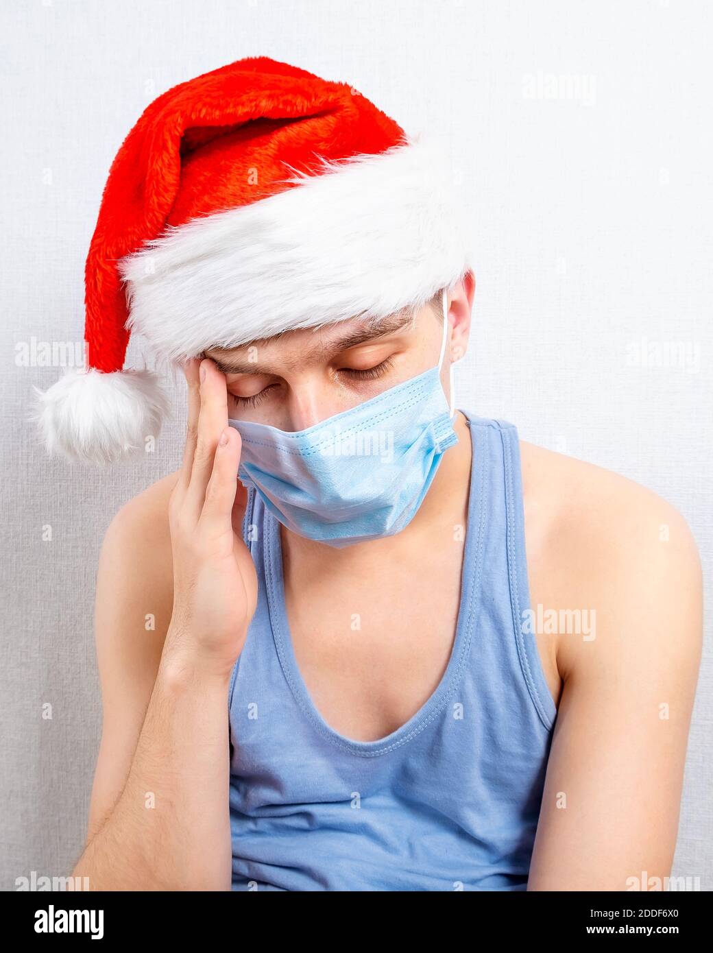 Trauriger junger Mann in Weihnachtsmütze und Grippe Maske von Die Wand im Raum Stockfoto