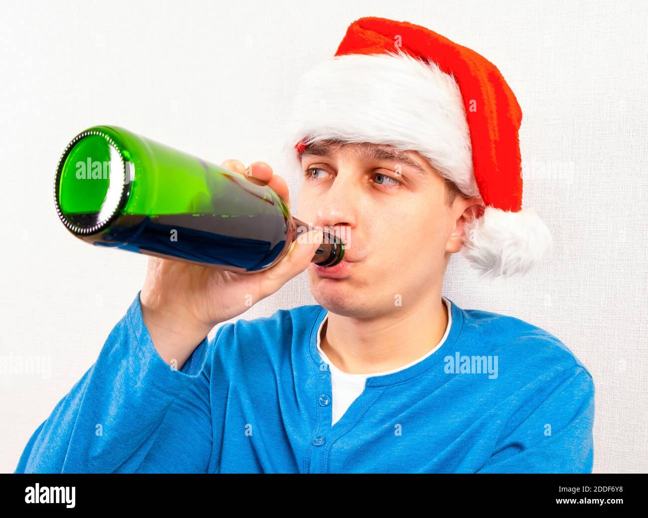 Junger Mann in Santa hat trinken ein Bier von der Wand im Zimmer Stockfoto