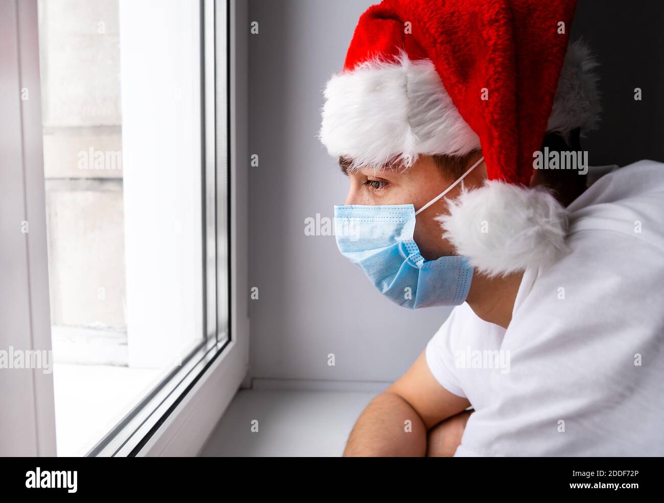 Nachdenklicher junger Mann in Santa hat am Fenster Stockfoto