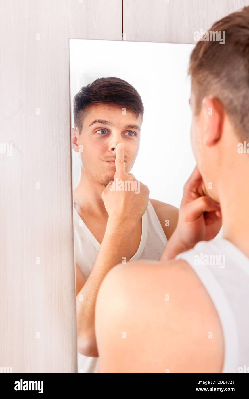 Junger Mann, der im Spiegel reflektiert und macht Ein lustiges Gesicht Stockfoto