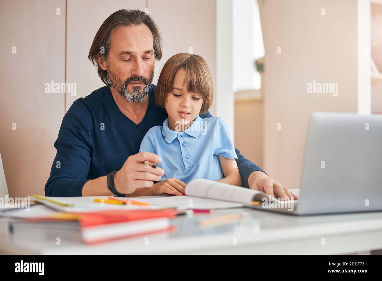 Fürsorglicher Vater hilft seinem Kind, Hausaufgaben zu bewältigen Stockfoto
