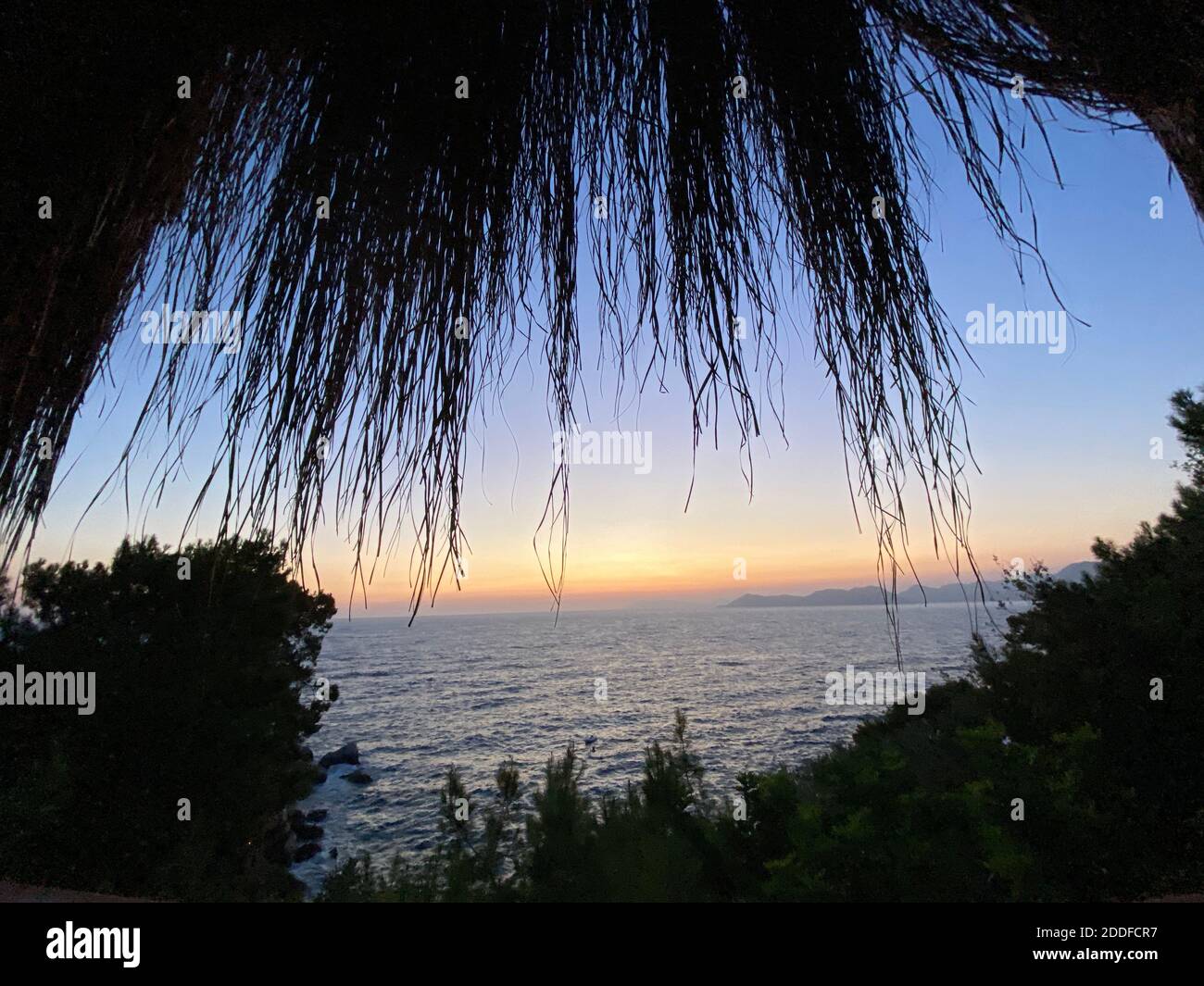 Schöner romantischer Sonnenuntergang auf der Ägäis mit Pinien und Hügeln am Horizont. Reflexionen der Morgendämmerung über dem Meer. Dramatische Farben des Himmels. Stockfoto