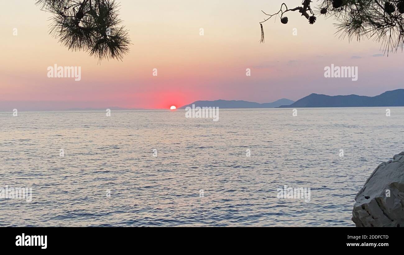 Schöner romantischer Sonnenuntergang auf der Ägäis mit Pinien und Hügeln am Horizont. Reflexionen der Morgendämmerung über dem Meer. Dramatische Farben des Himmels. Stockfoto