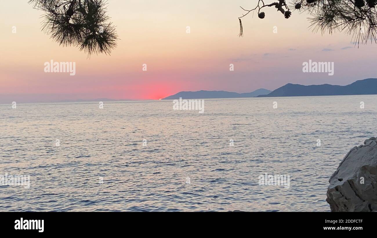 Schöner romantischer Sonnenuntergang auf der Ägäis mit Pinien und Hügeln am Horizont. Reflexionen der Morgendämmerung über dem Meer. Dramatische Farben des Himmels. Stockfoto
