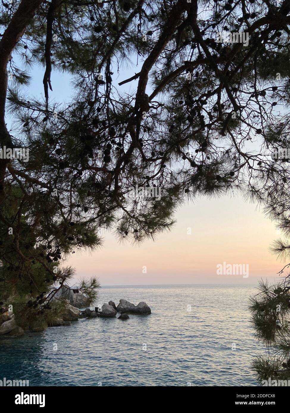 Schöner romantischer Sonnenuntergang auf der Ägäis mit Pinien und Hügeln am Horizont. Reflexionen der Morgendämmerung über dem Meer. Dramatische Farben des Himmels. Stockfoto