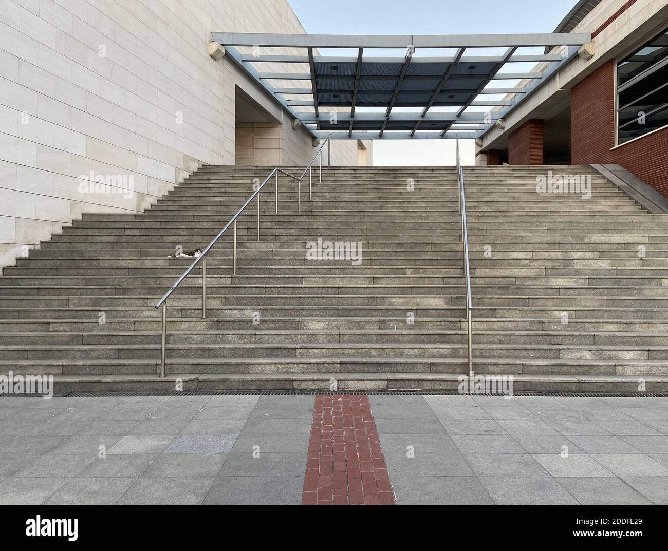 Betonsteinwände und Treppen mit Stahlschienen, modernes Architekturgebäude mit roten Ziegeln, Glasschirm, Katze sitzt auf der leeren Treppe. Stockfoto