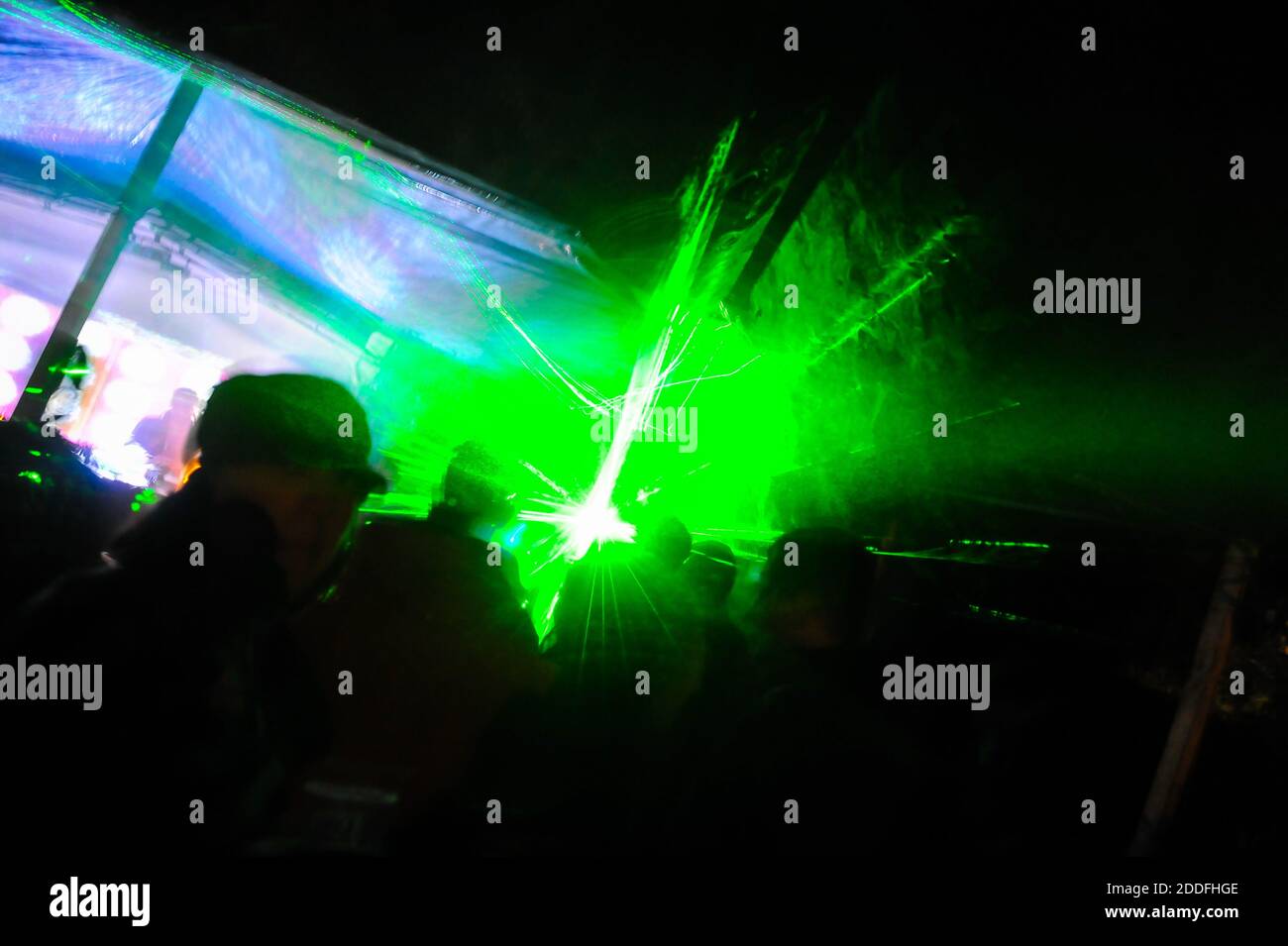 Trippiges Nachtbild mit tanzenden Menschen im Freien in einem Waldmusikfestival mit Laserstrahlen im Hintergrund. Stockfoto