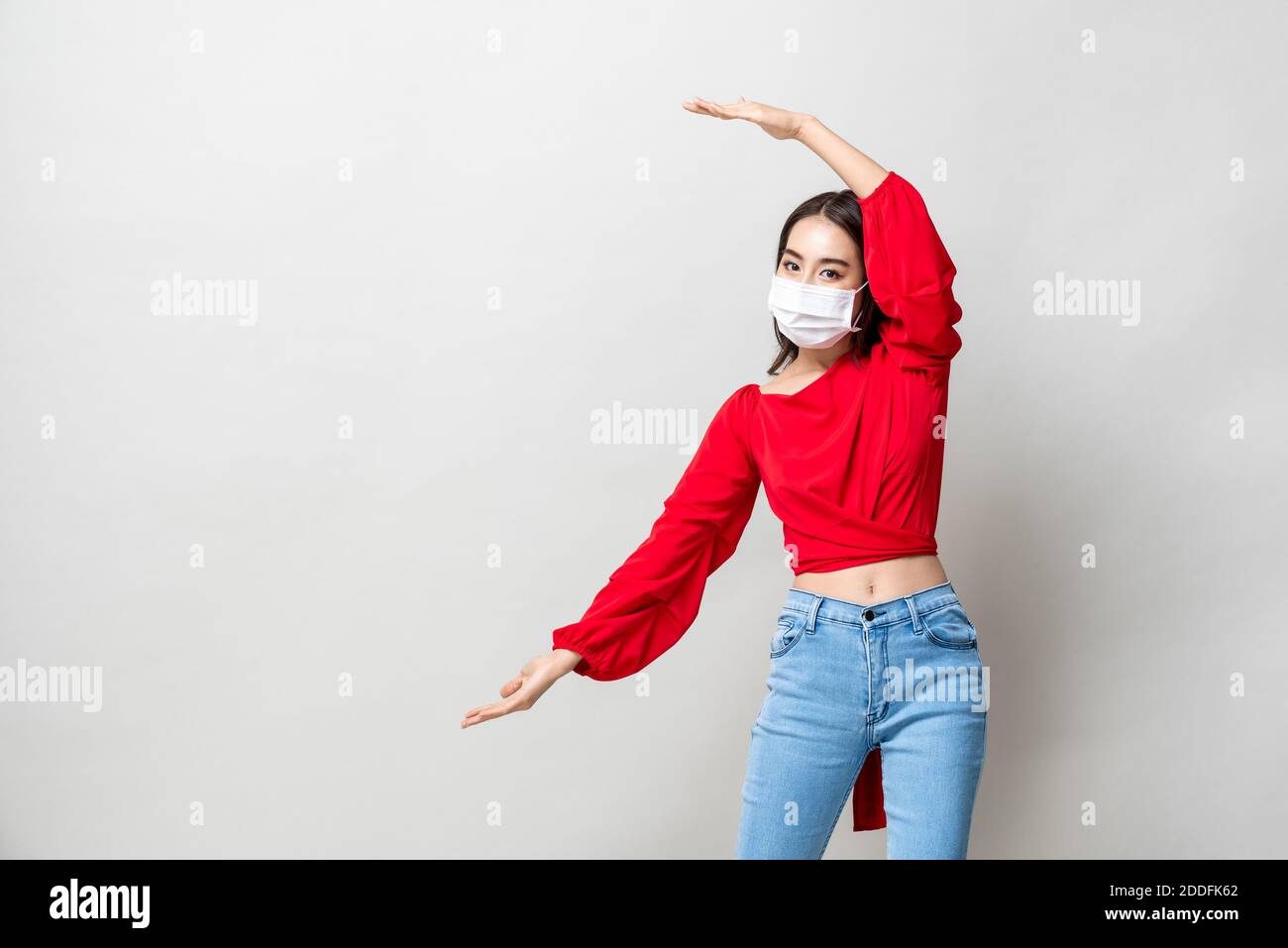 Asiatische Frau trägt medizinische Maske und offene Hände zu leeren Platz beiseite auf hellgrauem Studiohintergrund Stockfoto