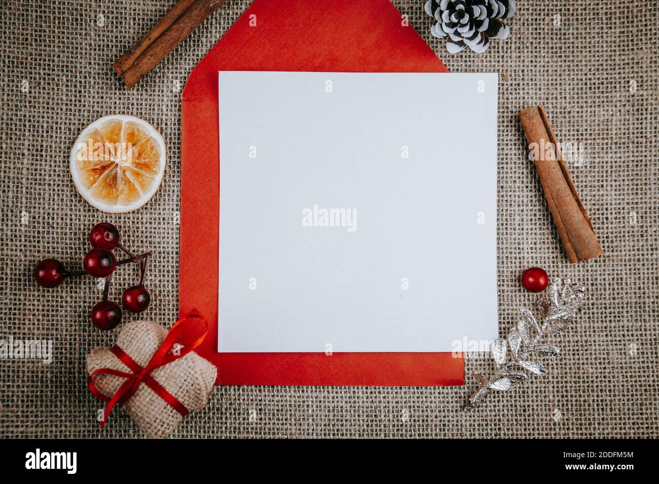 Mockup unbeschriftete Grußkarte, roter Umschlag, Geschenkbox, Zimtstangen. Draufsicht flach Lay gestylt Weihnachten mockup auf einem rustikalen rauen Leinen Hintergrund. Stockfoto