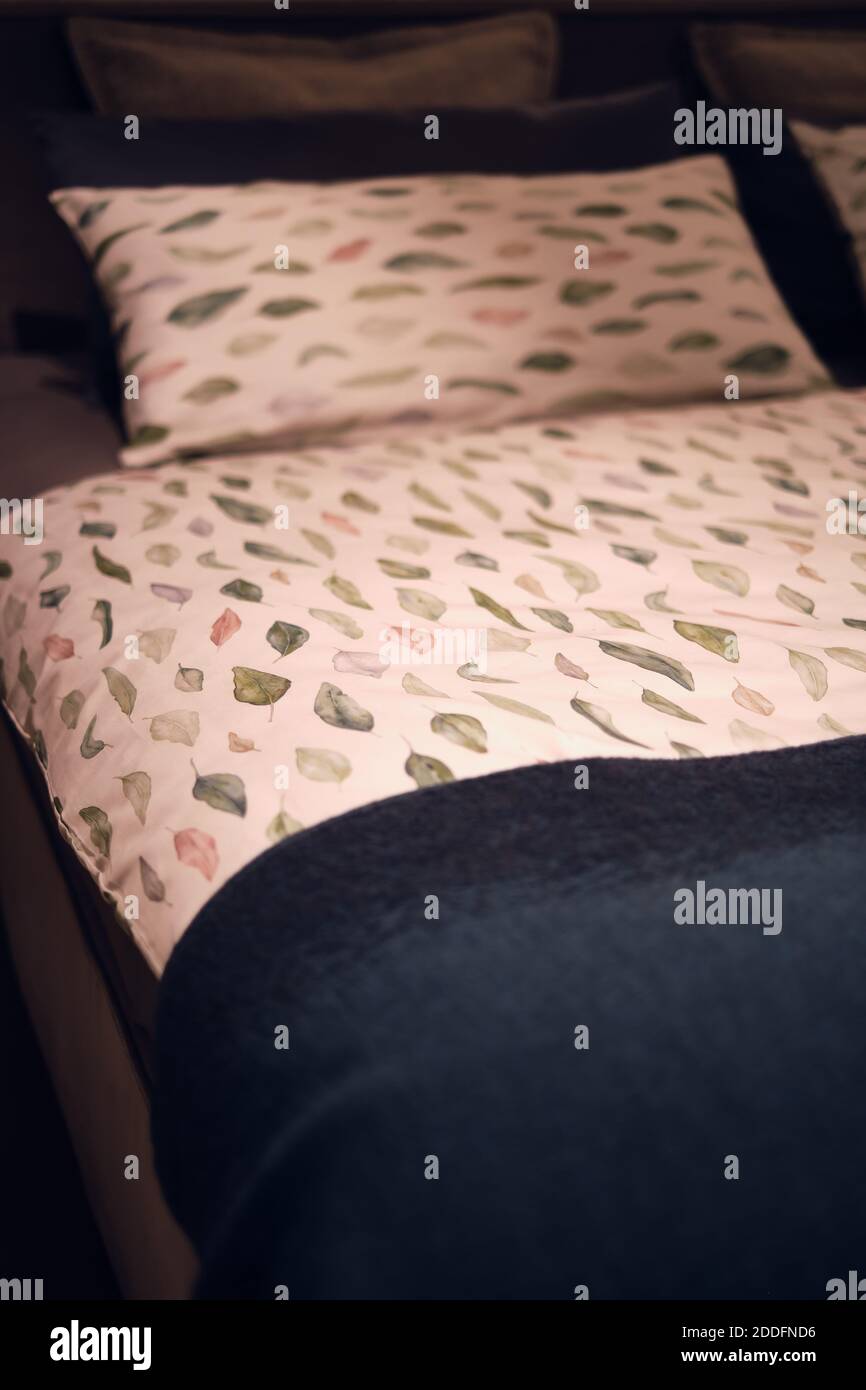 Bett und Bettwäsche, weiches weißes Kissen und Bettbezug mit dekorativem botanischem Muster, Herbstblättern und blauer Decke. Moderne Schlafzimmer. Stockfoto