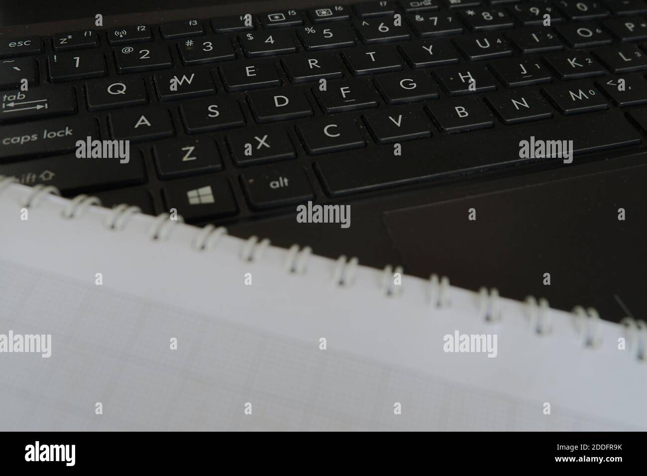 Ein High-Angle-Aufnahme eines schwarzen Tastatur-Laptops mit Ein offenes leeres Notizbuch Stockfoto