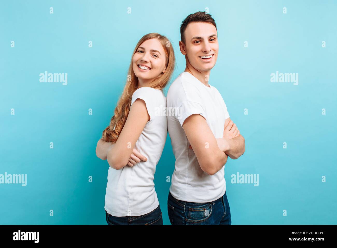 Glücklich liebendes Paar, Mann und Frau, in weißen T-Shirts gekleidet, Rücken an Rücken und lächelnd, vor blauem Hintergrund Stockfoto