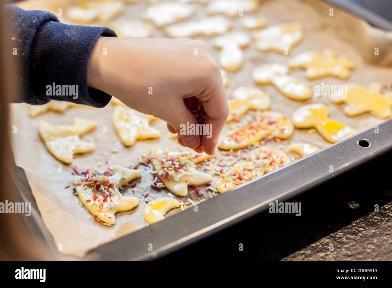 Bamberg, Deutschland 22. November 2020: Symbolbilder - 2020 - hausgemachtes Platzchen/Platzchen, in verschiedenen Formen ausgeschnitten, auf einem Backblech mit Backpapier liegen, der Keksteig wird von einem kleinen Mädchen mit Streuseln aus Zuckerperlen verziert. Weltweite Nutzung Stockfoto