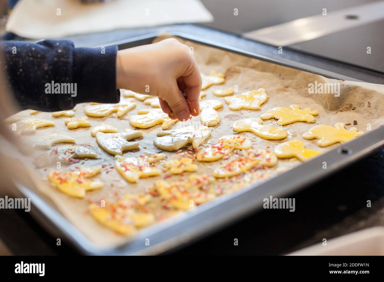 Bamberg, Deutschland 22. November 2020: Symbolbilder - 2020 - hausgemachtes Platzchen/Platzchen, in verschiedenen Formen ausgeschnitten, auf einem Backblech mit Backpapier liegen, der Keksteig wird von einem kleinen Mädchen mit Streuseln aus Zuckerperlen verziert. Weltweite Nutzung Stockfoto