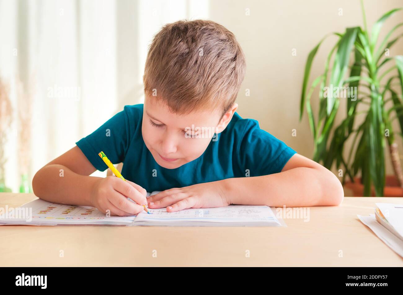 7 Jahre alter Junge, der Unterricht studiert, sitzt am Schreibtisch in seinem Zimmer. Stockfoto