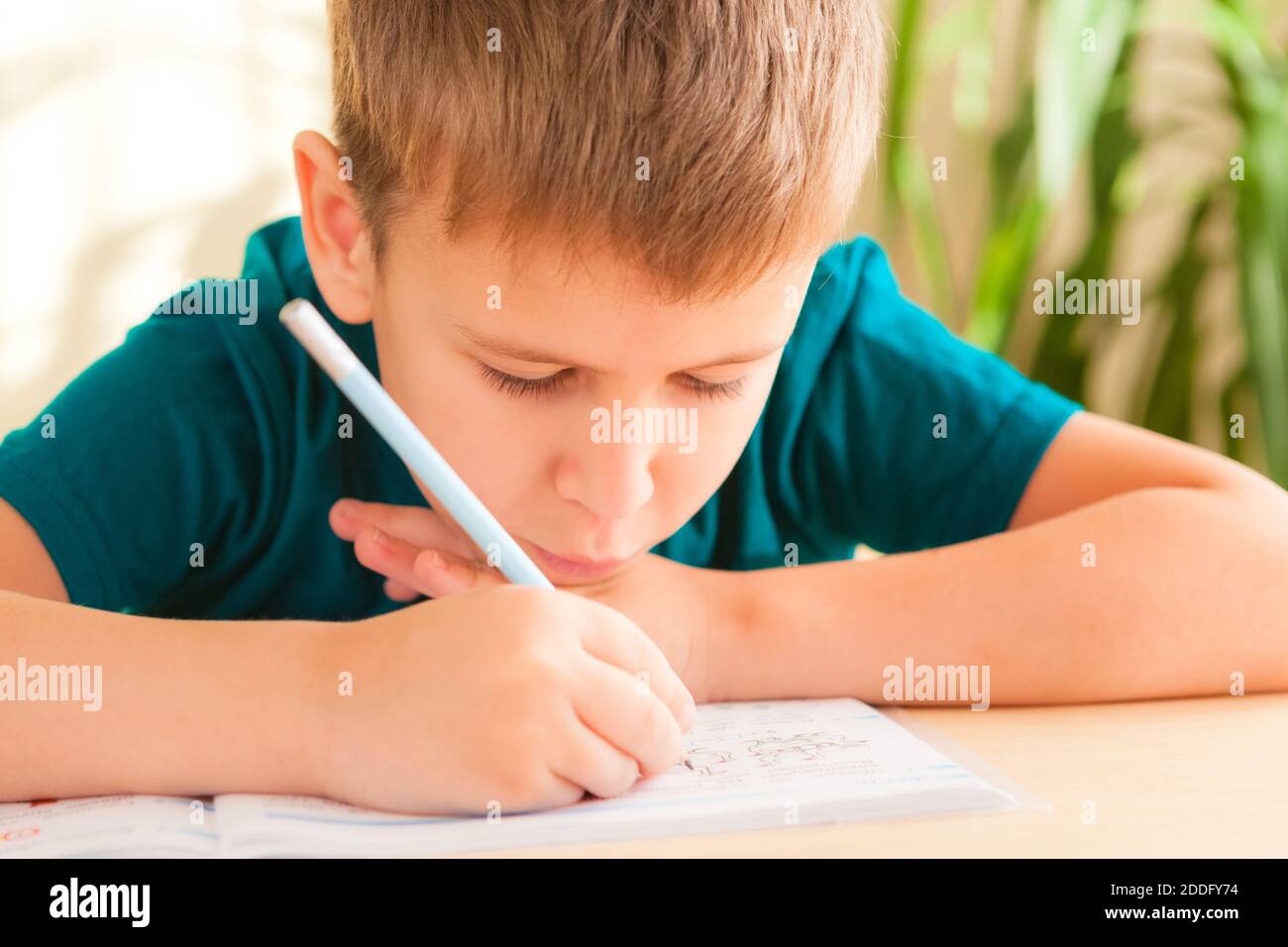 Nahaufnahme eines 7 Jahre alten Jungen, der Unterricht am Schreibtisch in seinem Zimmer macht. Stockfoto