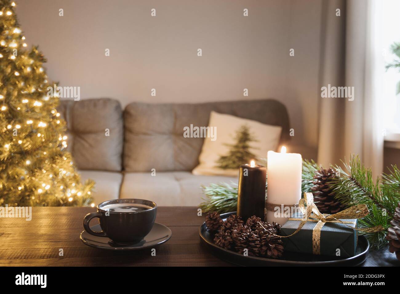 Gemütliches Interieur mit Weihnachtsbaum und warme Tasse Kaffee auf Holz-Tischplatte mit Kerzen, Geschenke Kegel im Wohnzimmer. Weihnachten Urlaub zu Hause. Stockfoto