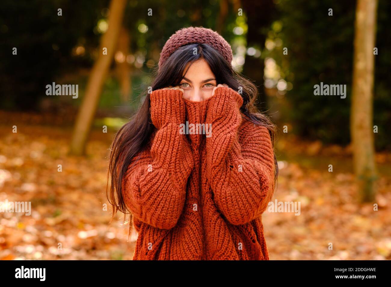 Junge Frau in gestrickten Hut über Gesicht mit warmen Pullover Während im Wald in kalten Herbsttag stehen Stockfoto
