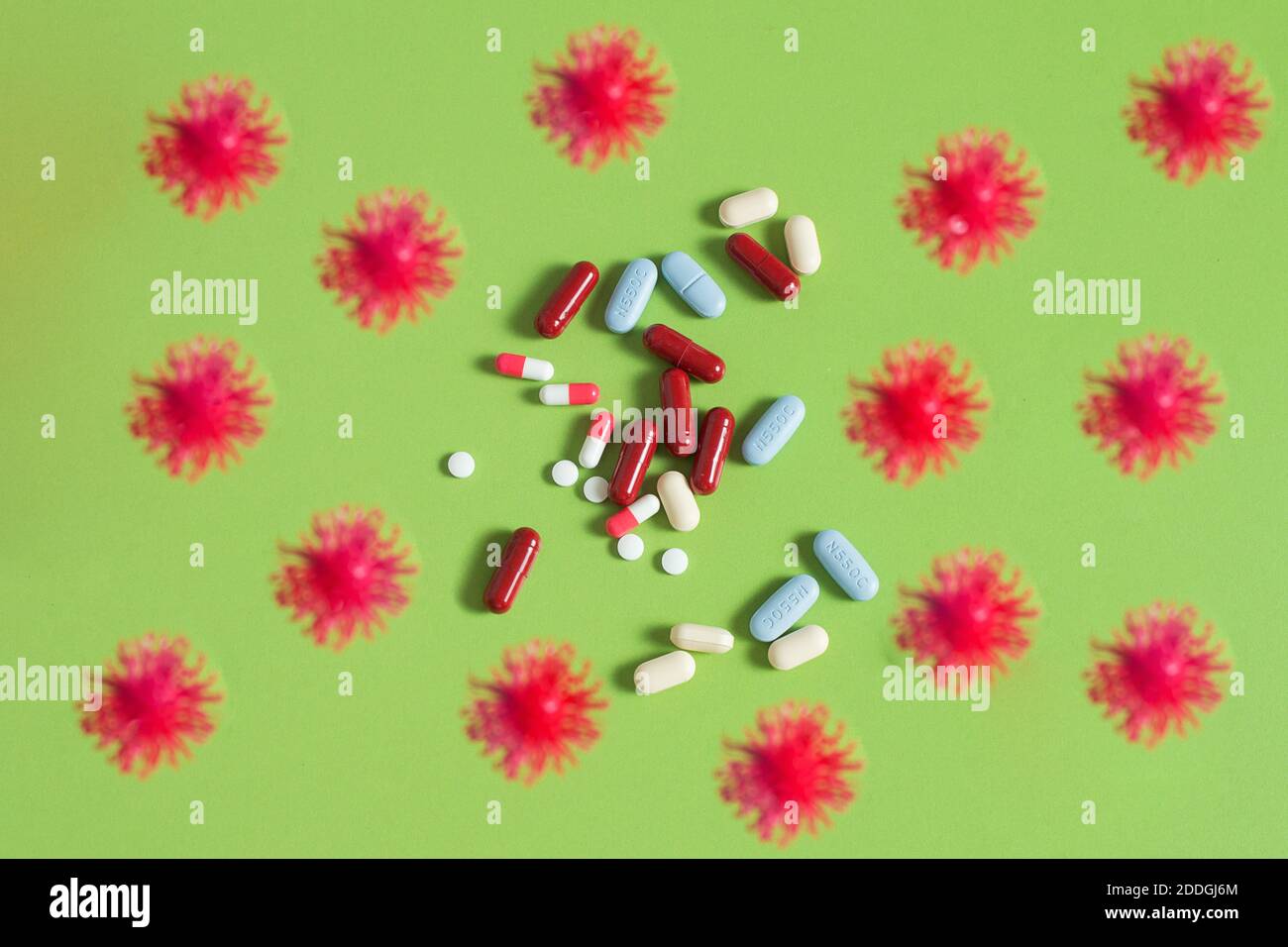 Viren umgeben einen Haufen Pillen auf einem grünen Tisch. COVID-19 Simulationspartikel mit einigen Medikamenten auf grünem Hintergrund. Gesundheitskonzept. Stockfoto
