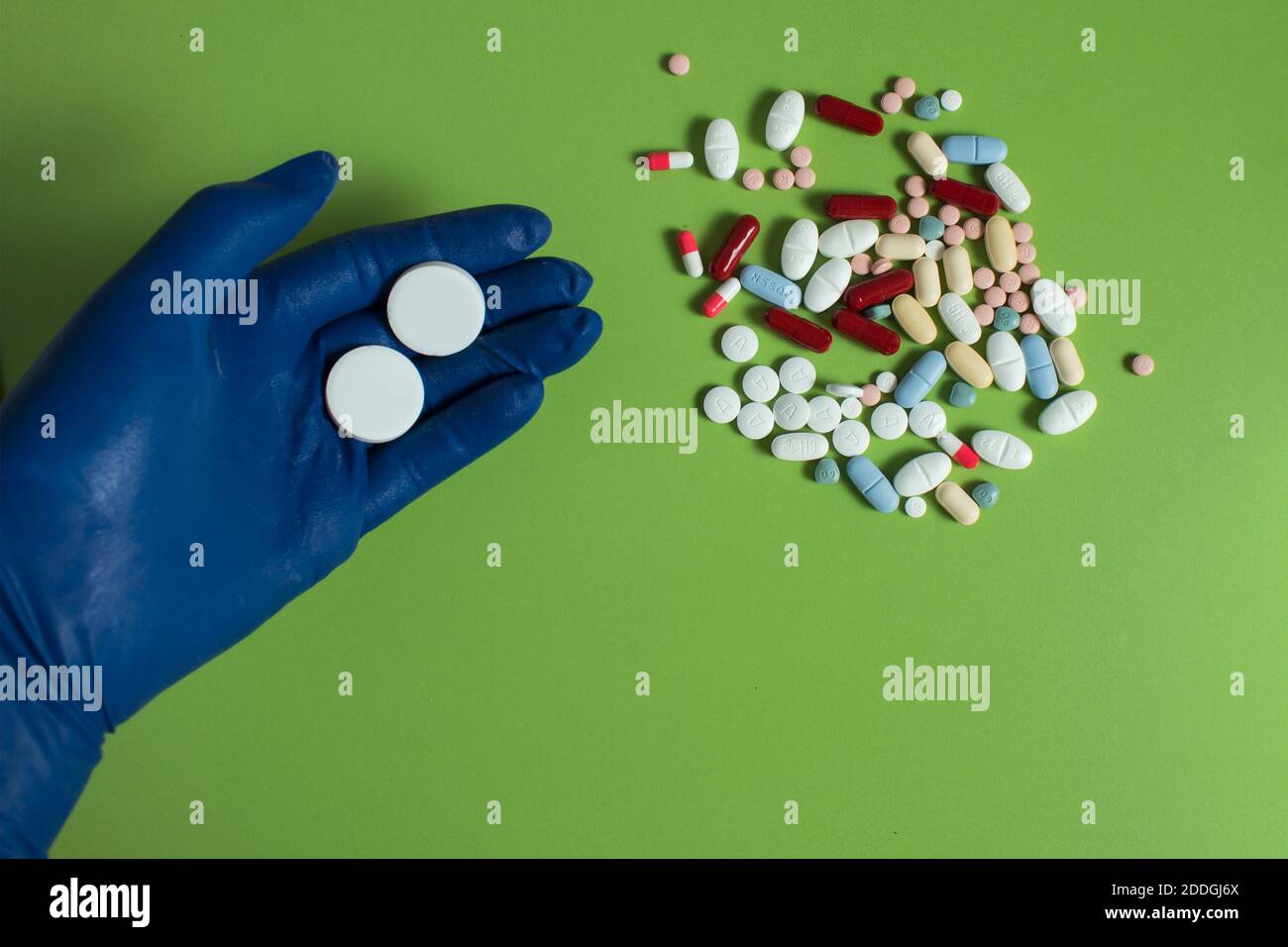Ein blauer Handschuh enthält zwei große runde Pillen in der Nähe einiger Medikamente auf einem grünen Tisch. Persönliche Schutzausrüstung. Stockfoto