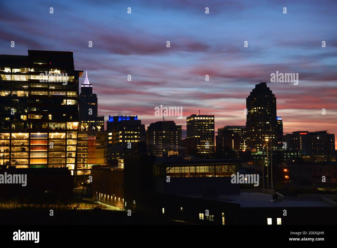 Die Lichter der Stadt sind immer noch an, wenn die Sonne aufgeht Im Osten und malt die Wolken orange während des Sonnenaufgangs Über der Innenstadt von Raleigh North Carolina Stockfoto