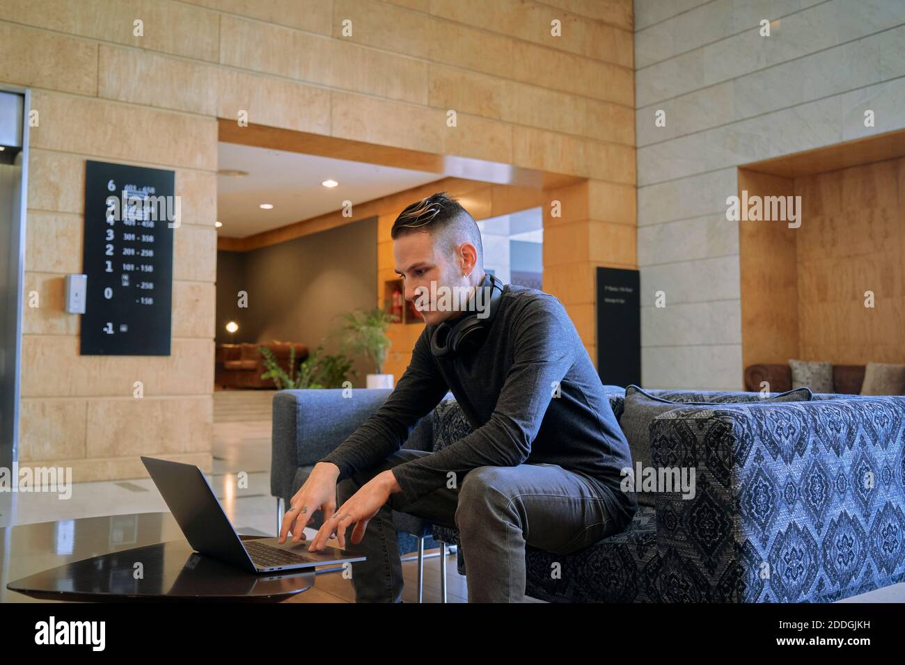 Seitenansicht des konzentrierten männlichen Unternehmers, der in einem Sessel sitzt Lounge des Hotels, während man einen Laptop benutzt und an einem Remote-Projekt arbeitet Stockfoto