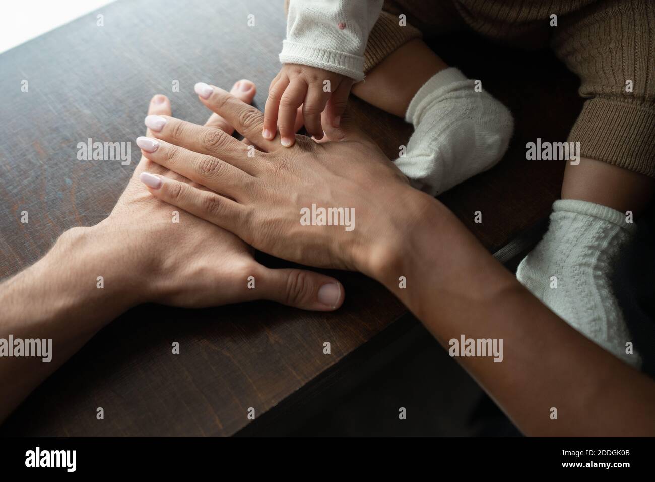 Hoher Winkel der Ernte unkenntlich multiethnischen Paar und Baby Putting Hände zusammen auf dem Tisch Stockfoto
