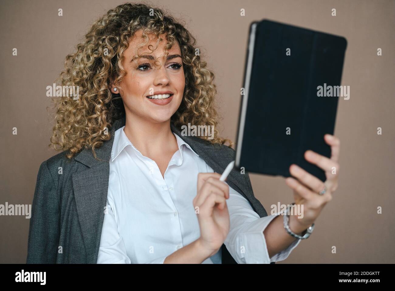 Fröhliche weibliche Unternehmerin in formellen Outfit mit Tablet mit Stift Und Freude über Projektabwicklung auf braunem Hintergrund im Studio Stockfoto