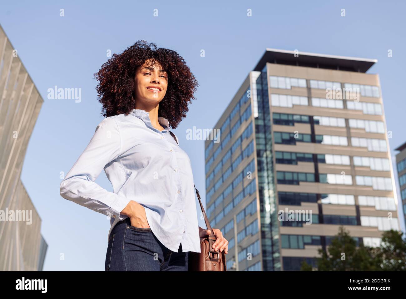 Low-Winkel-Seitenansicht der lächelnden Unternehmerin in smart Legeres Outfit, das in Megapolis entlang der Straße läuft und wegschaut Stockfoto